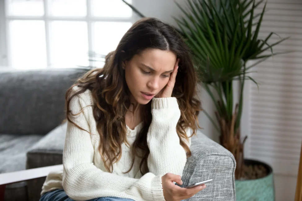 Young woman looking upset while reading a message on her phone